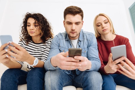 Online chatting. Serious girls looking at their telephones and leaning elbows on knees while being...