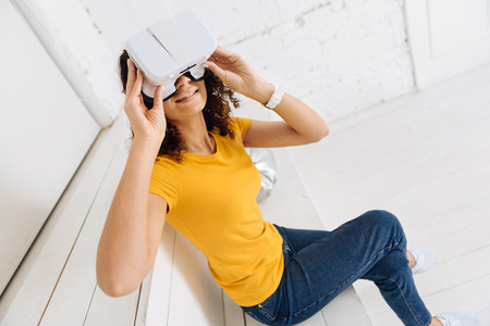 Turn on imagination. Attractive brunette keeping smile on her face and raising arms while touching her modern gadgetの写真素材