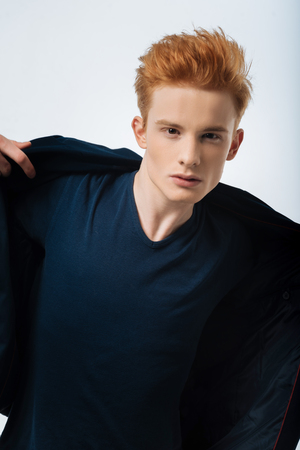 Dandy. Attractive humourless red-haired young man putting his jacket on and staring and looking seriouslyの写真素材