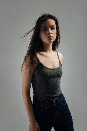 Young. Beautiful stony-faced dark-haired young woman thinking and looking in the distance and wearing a top and jeansの写真素材