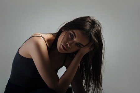 Upset. Pretty sad long-haired young woman sitting and thinking and holding her head with her handの写真素材