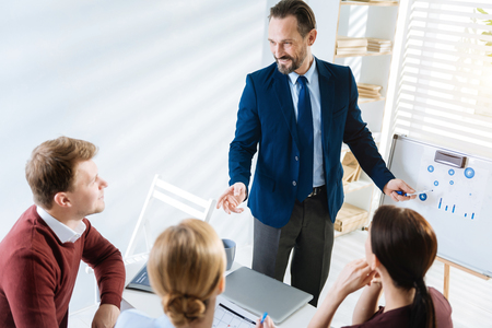 Crucial data. Top view of male colleague showing  plan while staring  at others and grinningの写真素材