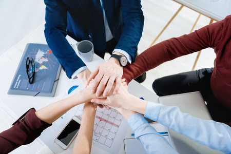 Team goal. Top view of young female and male hands hold above the table where documents and glasses lyingの写真素材