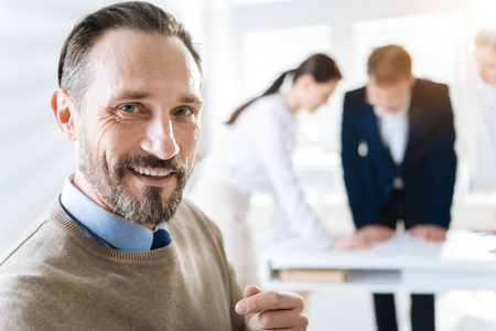 White smile. Portrait of charming sincere male colleague smiling and looking at the camera while standing on the blurred backgroundの写真素材