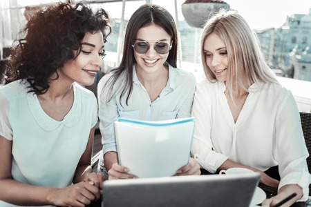 Funny files. Interested joyful pleasant girls looking at the screen of the laptop smiling and spending time together.の写真素材