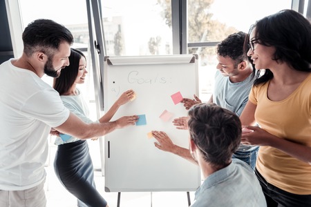 Getting organized. Positive minded coworkers sticking notes on a presentation board and smiling while talking about company goals in office.の写真素材