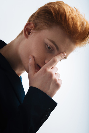 Consideration. Good-looking serious red-headed young man wearing a black jacket and touching his forehead and thinkingの写真素材