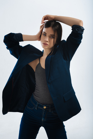 Life is move. Active determined confident woman posing on the white background and looking at the camera while caressing her hairの写真素材