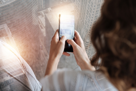 Quick message. Close up of a smart phone in hands of a pleasant woman using it while chattingの写真素材