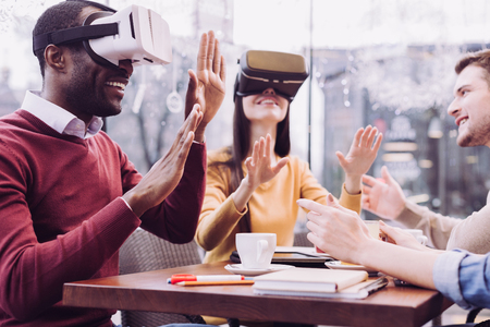 Digital technology. Happy positive two friends moving hands while trying VR handset and grinningの写真素材