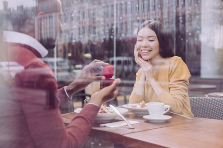 In love. Pleasant joyful loving man sitting at cafe and proposing woman who laughingの写真素材
