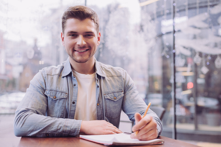 Complicated task. Pleasant joyful female student holding pencil while looking at the camera and smilingの写真素材