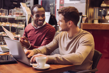 Favorite job. Ambitious skillful two colleagues working on laptop while sitting at cafe and communicatingの写真素材