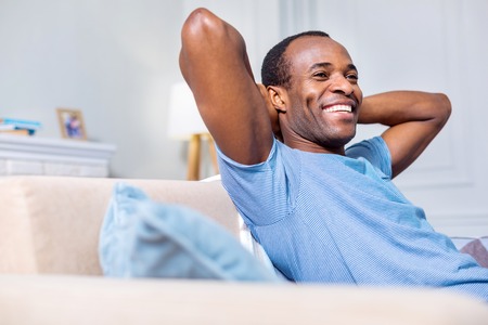 Pleasurable time. Joyful positive good looking man smiling and enjoying his rest while being at homeの写真素材