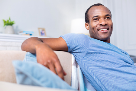 Pleasant emotions. Delighted joyful positive man smiling and feeling happy while enjoying his time at homeの写真素材