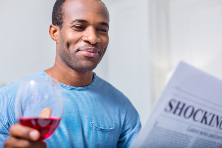Relaxing evening. Positive nice happy man smiling and looking at the newspaper while enjoying his restの写真素材