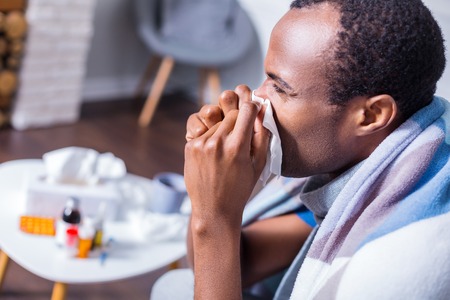 Unpleasant illness. Sad depressed cheerless man sneezing and feeling unwell while being sickの写真素材