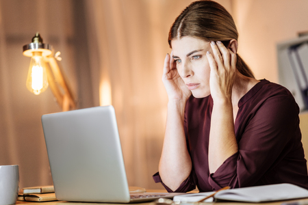 Try to concentrate. Attentive worker pressing lips and leaning elbows on table while looking at computerの写真素材
