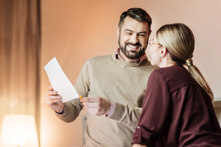 Pleasant conversation. Handsome man keeping smile on his face and pointing at document while looking at his partnerの写真素材