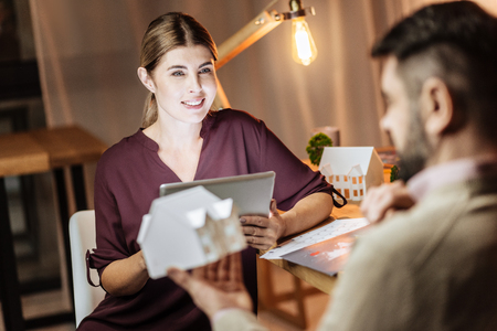 Interesting communication. Beautiful freelancer feeling happiness while talking with her friend and holding tablet in both handsの写真素材