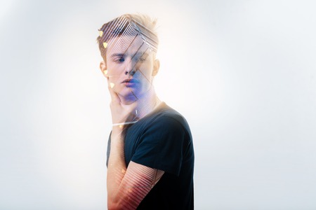 Fresh ideas. Creative thoughtful young man standing in the white room looking aside and holding hand near neck.の写真素材