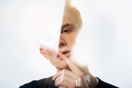 Do not speak. Handsome calm redhead man tilting head right looking aside and holding finger near mouth.の写真素材