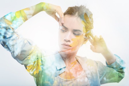 Nature is here. Creative beautiful thoughtful woman standing in the bright room holding hands near head and looking aside.の写真素材