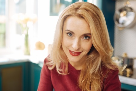 Good-looking inspired grey-eyed blond young woman smiling and wearing red lipstick and relaxingの写真素材
