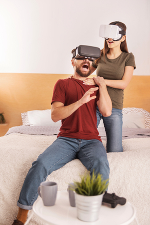 Technology innovation. Vigorous emotional young couple having fun with VR headsets while man screaming and gesturingの写真素材