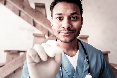 Let me check. Positive minded male doctor using a disposable wooden stick while visiting a patient and checking throat.の写真素材