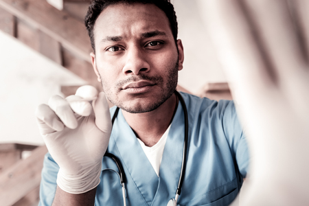 Looking serious. Concentrated millennial doctor using a wooden stick while checking his patient throat and making a diagnosis.の写真素材
