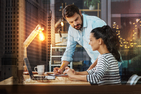 Reliable smart employer looking at his cheerful emotional new secretary and slightly leaning to the table while talking about the rights and duties in his companyの写真素材