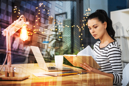 Reading notes. Calm clever responsible employee looking strict while sitting alone in her comfortable room and reading important notesの写真素材