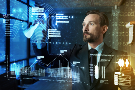 Digital world. Calm elegant attentive programmer feeling concentrated while looking at the transparent screen and thinking about the information on itの写真素材