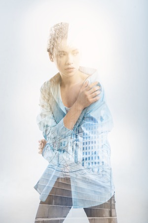 Cold afternoon. Sad young pretty woman standing alone and being cold while touching her shoulder and looking into the distanceの写真素材