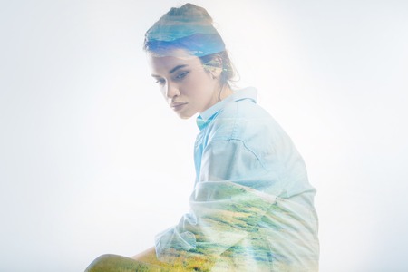 Gloomy thoughts. Beautiful young woman being in a gloomy mood and thoughtfully looking down while sitting alone in her roomの写真素材