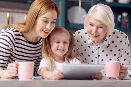 Funnier together. Petite little girl showing a video on the tablet to her mother and grandmother...