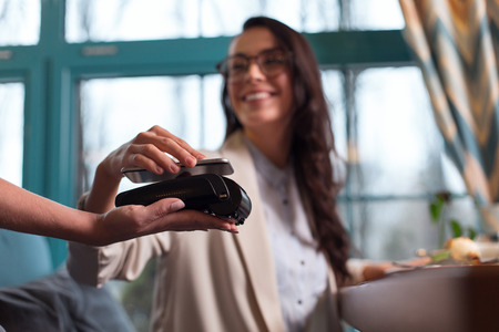 Payment with smartphone. Selective focus of bank terminal carried by female hand and woman using smartphone for paying checkの写真素材