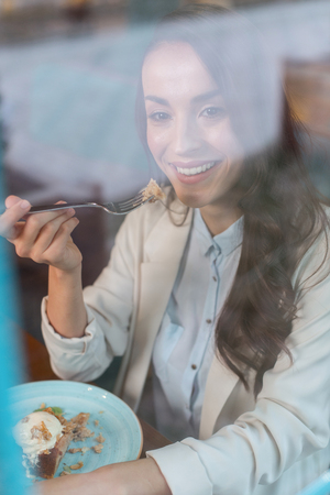 Best dessert. Top view of merry carefree sincere woman smiling while eating dessert and enjoying itの写真素材