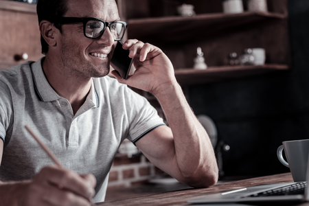Work is calling. Positive minded millennial guy smiling while taking some notes and having a pleasant conversation with his business partner.の写真素材