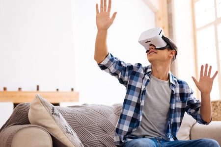 Relaxing at weekend. Cheerful well-built stylish adolescent wearing a VR headset and relaxing while...
