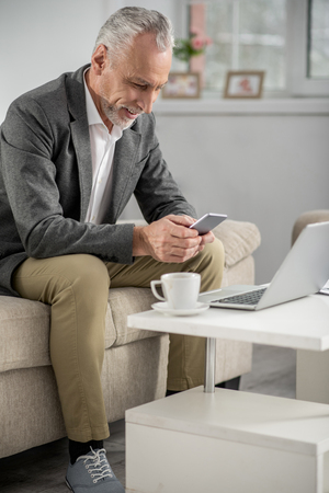 Have a look. Attentive man sitting on his sofa and bowing head while using his gadgetの写真素材