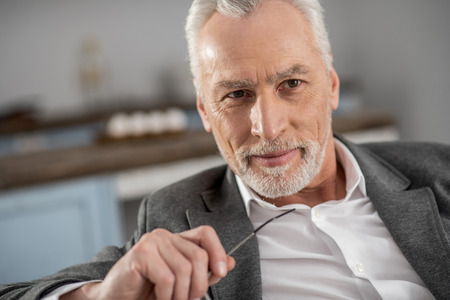 Facial expressions. Mature male person expressing positivity while looking aside, being at homeの写真素材