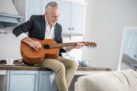 It is my hobby. Handsome man keeping smile on his face and bowing head while looking at his instrumentの写真素材