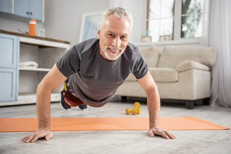Sporty mood. Positive delighted retirement keeping smile on his face and doing push-ups while taking care of his healthの写真素材