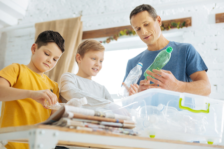 Caring about nature. Charming young man and his pre-teen sons preparing plastic bottles for recycling, crushing the bottles and putting them into special containersの写真素材