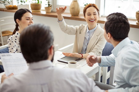 Telling stories. Pretty exuberant red-haired young woman smiling and gesturing while telling a story to her friendsの写真素材