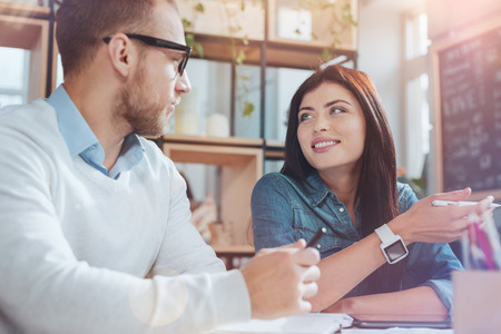 Lets consult. Positive delighted colleagues keeping smile on faces and having interesting conversation while sitting opposite each otherの写真素材