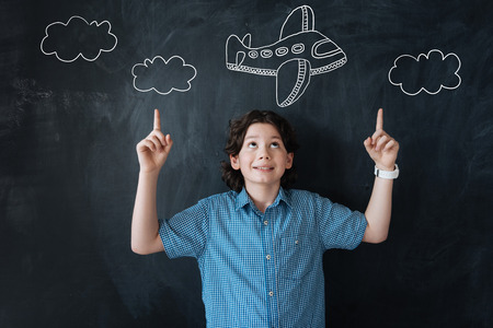 Lets fly. Excited cheerful little boy pointing to the sky while dreaming of travelling by planeの写真素材