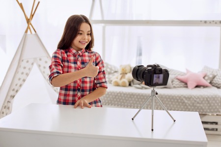 Best mood. Pretty pre-teen girl in a checked shirt filming a video blog and showing a thumbs up...